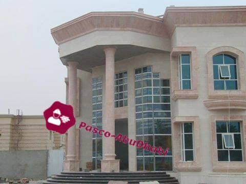 واجهة فيلا بالحجر الوردي المائل للبيج مع أعمدة دائرية وواجهة زجاجية